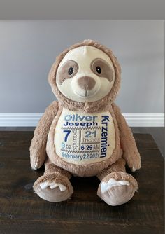 a teddy bear with a birth announcement on it's chest sitting on a wooden floor