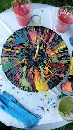 a table topped with paint and supplies on top of a grass covered field next to drinks