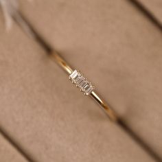 a diamond ring sitting on top of a piece of cardboard with a feather in the background