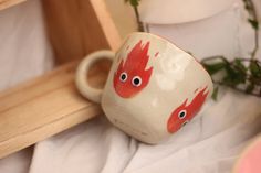 a red and white coffee cup with eyes on it sitting in front of a plant