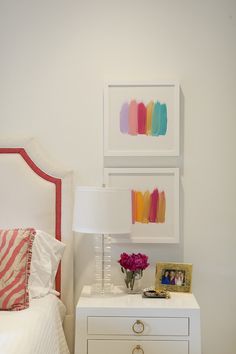 a white nightstand with two pictures on it next to a pink and yellow flower vase