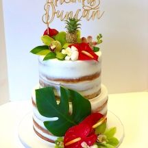 a three tiered cake with pineapples, flowers and leaves on the top