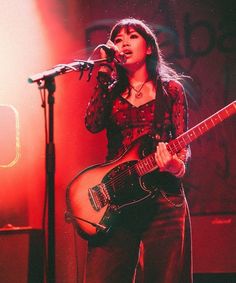 a woman singing into a microphone while holding a guitar