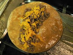 an uncooked tortilla sitting on top of a stove with cheese and other toppings