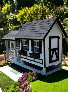 a small white and black house in the middle of a yard with flowers around it