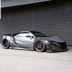 a silver sports car parked in front of a garage door with black rims on it