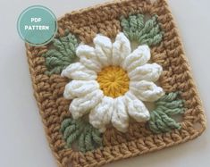 a crocheted square with a white flower on the center and green leaves around it