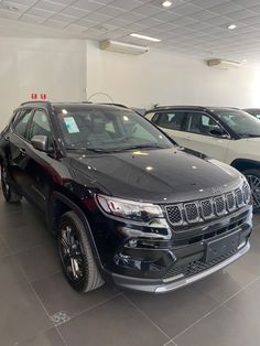 two jeeps are parked in a showroom next to each other and one is black