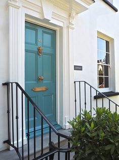 a blue front door on a white house with black railings and potted plants