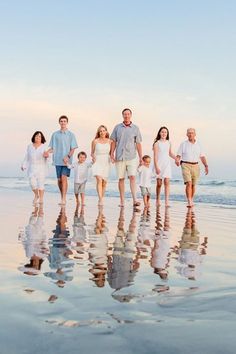 a family walking on the beach with their reflection in the wet sand and water at sunset