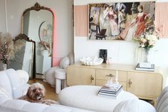 a dog is sitting on the couch in front of a mirror and table with flowers