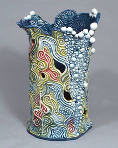 a blue vase with white balls on the top and an artistic design in the bottom