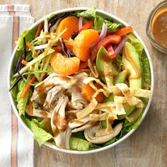 a salad with chicken, lettuce, carrots and avocado in a bowl