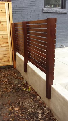 a wooden slatted fence next to a sidewalk with leaves on the ground in front of it