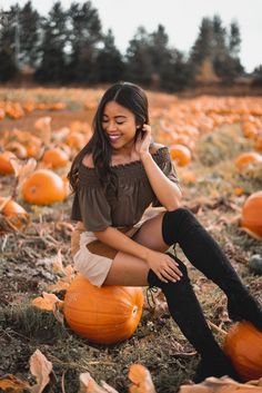 a woman sitting on top of a pumpkin field with her cell phone to her ear