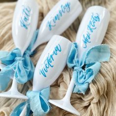 three white wine glasses with blue bows and name written on them, sitting next to each other