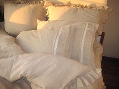 a bed with white linens and ruffled pillow cases on top of each other