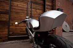 a silver motorcycle parked in front of a wooden building with a metal bar on it's back end