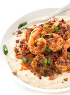 a white plate topped with mashed potatoes covered in shrimp and green onions next to a fork