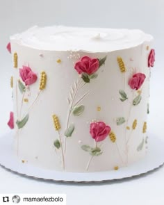 a white cake decorated with pink flowers and green leaves on a plate in front of a white background