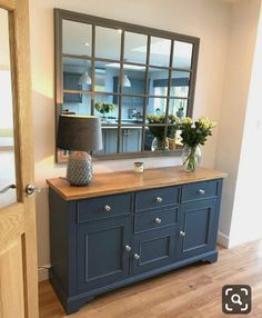 a blue dresser with flowers on top and a mirror behind it in a living room