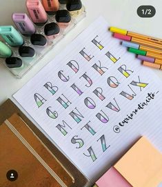 an open notebook with letters and numbers drawn on it next to colored crayons