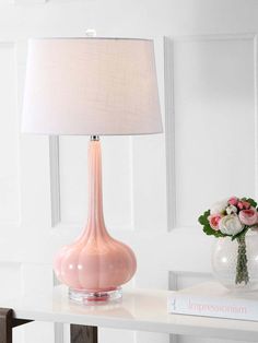 a pink lamp sitting on top of a white table next to a vase with flowers