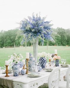 a white table topped with blue and white vases filled with flowers on top of a lush green field