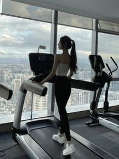 a woman standing on a treadmill in front of a window with cityscape