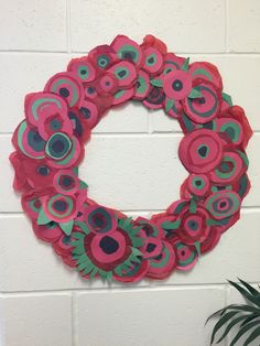 a paper flower wreath hanging on a white brick wall next to a potted plant