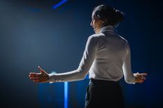 a woman in white shirt and black skirt standing on stage with her hands out to the side