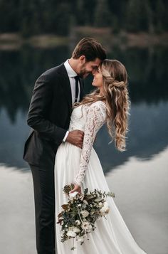 a bride and groom standing next to each other in front of water