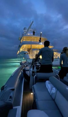 two people sitting on the back of a boat in the ocean at night, looking out to sea