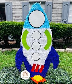 a rocket ship made out of legos sitting in the grass next to some bushes