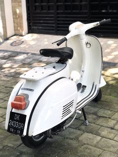 a white scooter parked in front of a garage door on a brick sidewalk