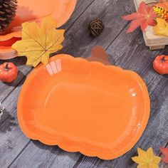 an orange plate sitting on top of a wooden table next to autumn leaves and acorns