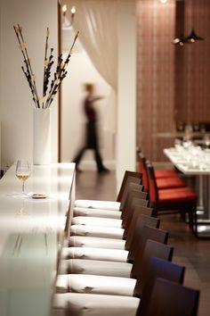 there is a vase with flowers in it on the long table next to chairs and a person walking by