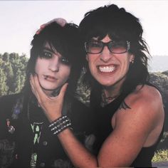 two women with black hair and glasses posing for a photo together in front of trees