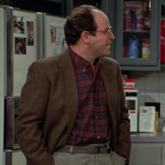 two men standing next to each other in a kitchen with refrigerators and cabinets behind them