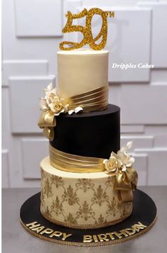 a 50th birthday cake decorated with gold and black frosting, flowers and ribbon on top