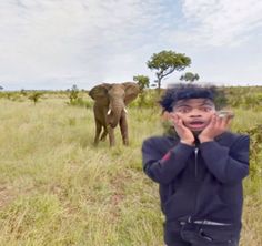 a young boy standing in the middle of a field with an elephant behind him,