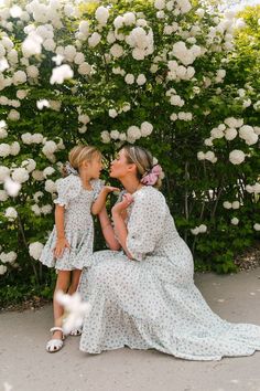 mother and daughter sitting on the ground in front of white flowers with their mouths open