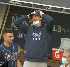 a man wearing a face mask while standing next to another man in front of a baseball dugout