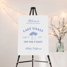 a white sign sitting on top of a easel next to a vase filled with flowers