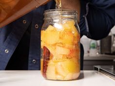 a person pouring liquid into a jar filled with fruit