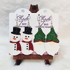 "Christmas Shaped faux leather earrings feature an adorable Snowman and Gnome! The Snowman has a black hat that can be glitter or solid and the scarf can be made in any color you wish, glitter or solid. The Gnome's hat can be customized to you color choice, also in glitter or solid.  Size: 2\" length x 1.1\" wide, with a 2.75\" drop (contact me if you want a different size) Shown is Snowman with black glitter hat and red glitter scarf, Gnome with green and red glitter hat." Faux Leather Christmas Earrings, Glitter Hat, Leather Christmas, Cricket Projects, Gnome Hat, Leather Ideas, Faux Leather Earrings, The Snowman, Bow Earrings