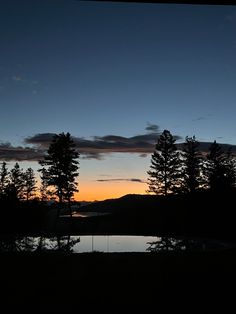 the sun is setting behind some trees and water