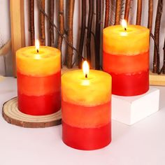 three red and yellow candles sitting next to each other on a white counter top with sticks in the background