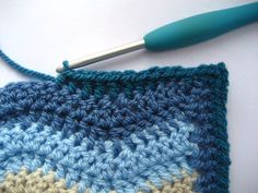 a crocheted square with a blue handle on top of it and a knitting needle in the middle