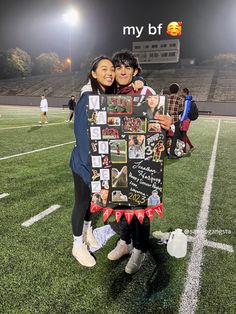 two people standing on a football field holding up a sign with photos attached to it